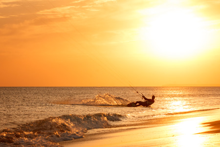 extreme professional kiter rides waves, jumps air on black sea with sail wing in hands led wind an sunset, onlookers photographers seagull on shore. village of annunciation. backlit, tonedの写真素材
