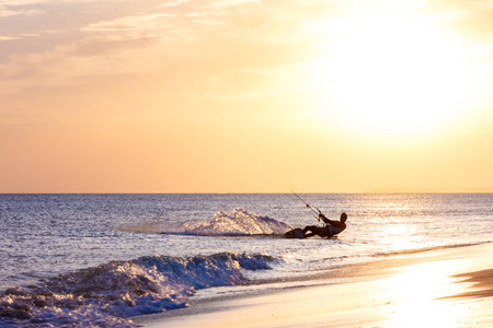 extreme professional kiter rides waves, jumps air on black sea with sail wing in hands led wind an sunset, onlookers photographers seagull on shore. village of annunciation. backlit, tonedの写真素材