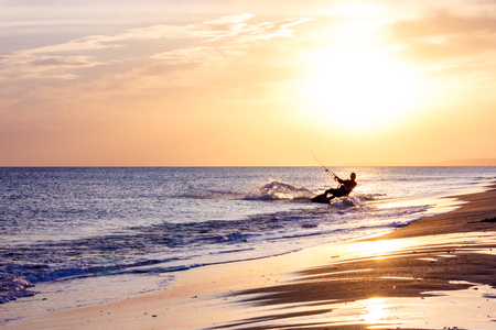 extreme professional kiter rides waves, jumps air on black sea with sail wing in hands led wind an sunset, onlookers photographers seagull on shore. village of annunciation. backlit, tonedの写真素材