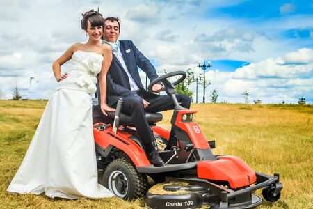 RUSSIA, YAROSLAVL -  19 JULY. 2012: The bride and groom run away from the master of ceremonies on a lawn mower across the field on a sunny day.のeditorial素材