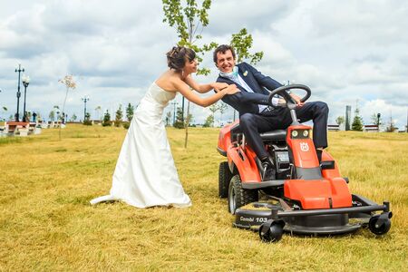 RUSSIA, YAROSLAVL -  19 JULY. 2012: The bride and groom run away from the master of ceremonies on a lawn mower across the field on a sunny day.のeditorial素材