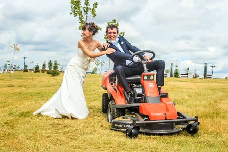 RUSSIA, YAROSLAVL -  19 JULY. 2012: The bride and groom run away from the master of ceremonies on a lawn mower across the field on a sunny day.のeditorial素材