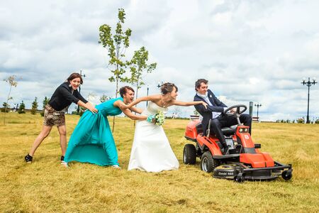 RUSSIA, YAROSLAVL -  19 JULY. 2012: The bride and groom run away from the master of ceremonies on a lawn mower across the field on a sunny day.のeditorial素材
