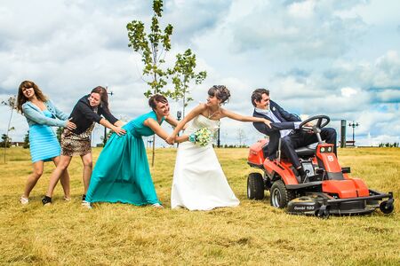 RUSSIA, YAROSLAVL -  19 JULY. 2012: The bride and groom run away from the master of ceremonies on a lawn mower across the field on a sunny day.のeditorial素材