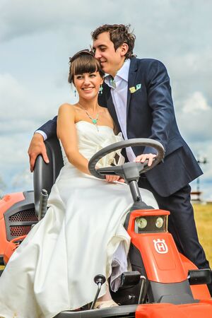 RUSSIA, YAROSLAVL -  19 JULY. 2012: The bride and groom run away from the master of ceremonies on a lawn mower across the field on a sunny day.のeditorial素材