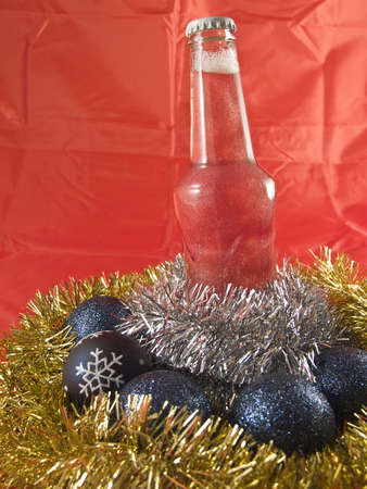 A selection of christmas ornaments and tinsel with a bottled drinkの写真素材