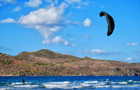 A kitesurfer has the time of his life riding the ocean waves on a sail full of windの写真素材