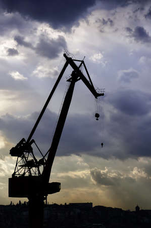 A dockyard crane is silhouetted against a dramatic evening sky.