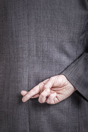 A conceptial image of a business man with his fingers crossed behind his back.の写真素材