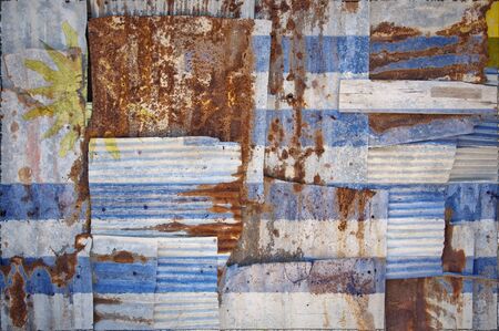 An abstract background image of the flag of Uruguay painted on to rusty corrugated iron sheets overlapping to form a wall or fence.の写真素材