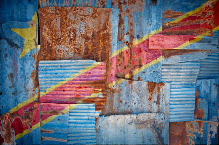 An abstract background image of the flag of Congo Kinshasa painted on to rusty corrugated iron sheets overlapping to form a wall or fence.の写真素材