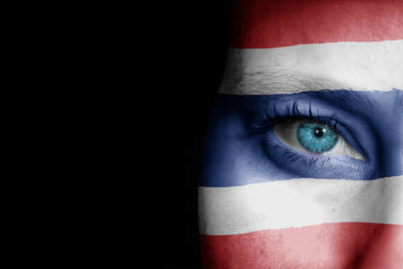 A young female with the flag of Thailand painted on her face on her way to a sporting event to show her support.の写真素材