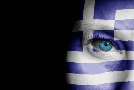 A young female with the flag of Greece painted on her face on her way to a sporting event to show her support.の写真素材