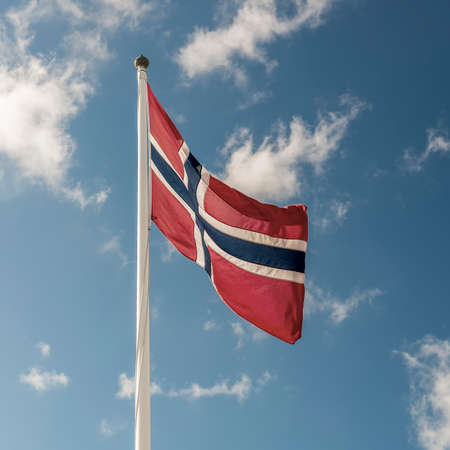 A Norwegian flag flutters in the wind against a blue sky backgroundの写真素材