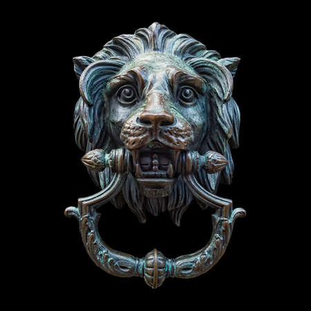 A classic lion head door knocker made out of metal and isolated against a black background.