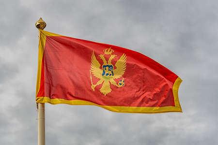 The flag of Montenegro fluttering in the wind against a cloudy sky background.の写真素材