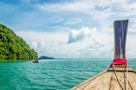 Tip of a traditional Thai transportation boat with a view of sea and and an island on a cloudy dayの写真素材