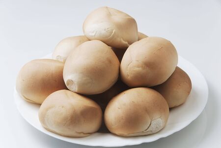 Stack of freshly-baked rolls on white plate; shot against white background