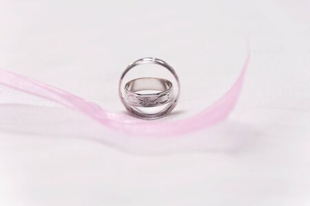 Silver wedding rings with pink ribbon on foreground
