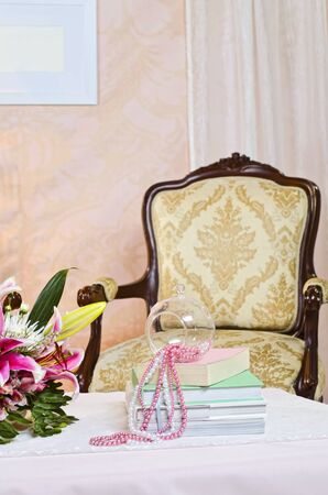 Studio setup of chair and coffee table with books, pearls, and flowers on topの写真素材