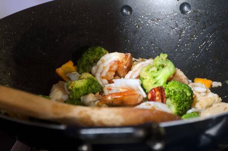 Close-up of shrimps and vegetables in wok with wooden spoonの写真素材