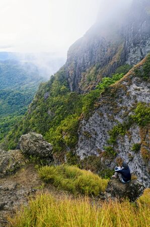 Young man in foggy mountain sitting on a rock by the cliffの写真素材
