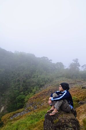 Young man in foggy mountain sitting on a rock by the cliffの写真素材