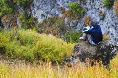 Young man sitting on mountain rock by the cliffの写真素材