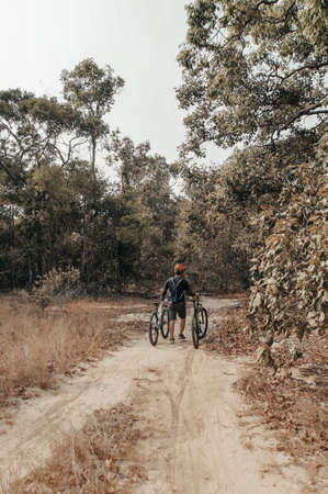 Rear view of a young man walking in the forest with him bicycleのeditorial素材