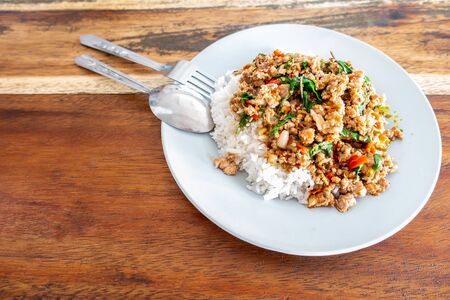 Rice topped with stir-fried pork and basil in  white dish on wooden table.の写真素材