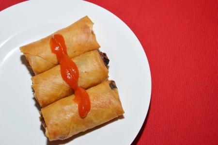 three spring rolls with chili sauce on a white plate