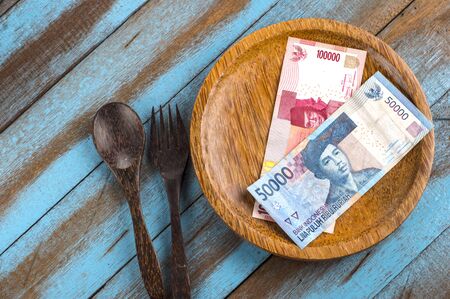brown wooden spoon and fork as well as the Indonesian currency banknotes on the wooden plate,...