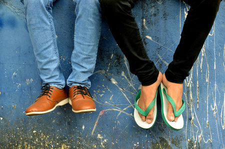 leather shoes and flip-flops with jeans on concrete wall