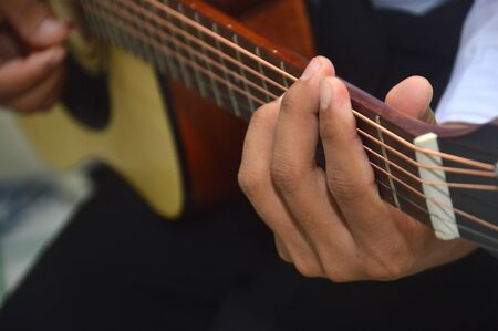 man's fingers playing a classical wooden guitar string