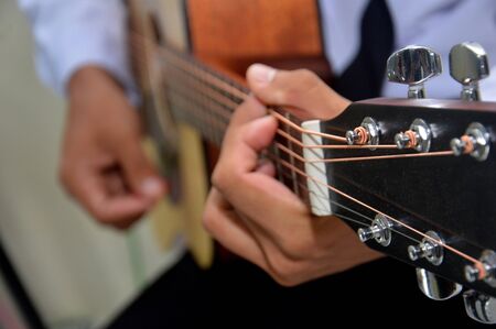 man's fingers playing a classical wooden guitar string