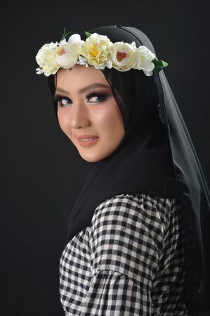 Portrait Beautiful Muslim Asian Girls with a checkered motif, a hijab with flower headbands, a photo in a studio on a black backgroundの写真素材