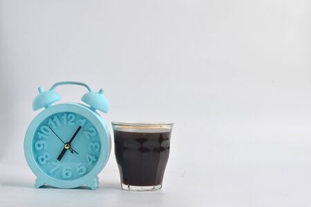A glass of black coffee and a blue alarm clock isolated on white background, coffee time concept