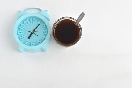A glass of black coffee and a blue alarm clock isolated on white background, coffee time conceptの写真素材
