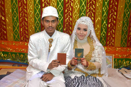 TARAKAN - INDONESIA 15 NOVEMBER 2017 : Indonesian bridal couples are happy and wearing white kebaya show their marriage book which is brown and greenのeditorial素材