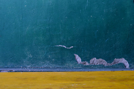 A textured teal wall featuring peeling plaster meets a vibrant yellow wooden floor creating a striking contrast. Perfect for backgrounds, design elements, or conveying a sense of urban decay.の写真素材