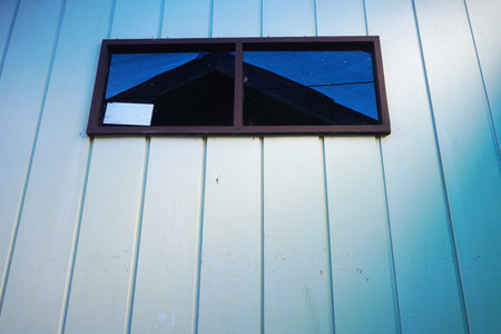 A simple window on a pale blue wall offers a striking reflection of the deep blue sky and a dark...