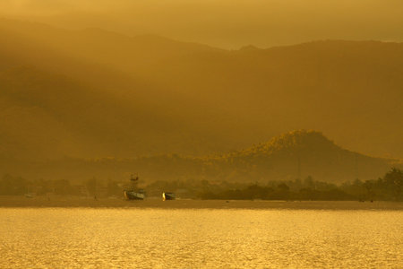Experience the serene beauty of sunrise over calm ocean waters with fishing boats near majestic mountains. Ideal for travel and relaxation themes.の写真素材
