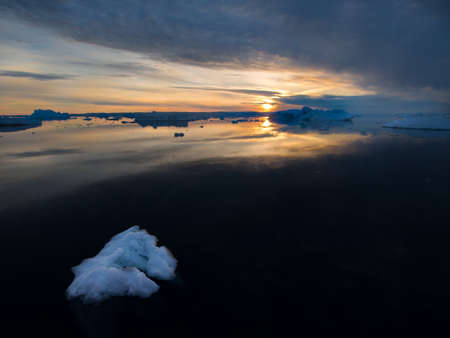 A piece of broken ice in foreground drifts in a dark black sea as a sun sets on the horizon amongst icebergs cause by global warming.Greenland Arctic.Imageの写真素材