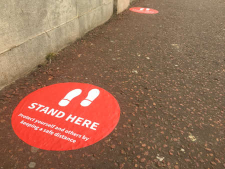 Red signs on a pavement indicate where people should stand to keep themselves and others safe by social distancing in national emergency against coronavirus.Imageの写真素材