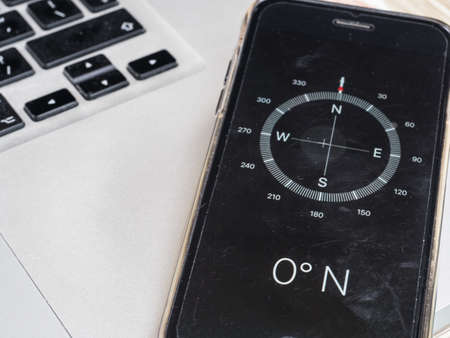 A compass on a smart phone indicates zero degrees North. Other compass points are seen blurring into distance. The phone sits on the corner of a computer keyboard.Technologyの写真素材