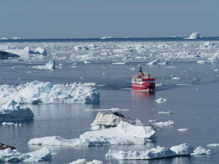 A red and white ship navigates its way between drifting ice floes.Ice bergs can be seen on the...