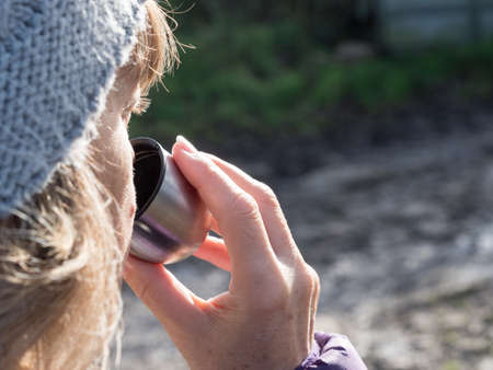 Close up of a lady wearing a bobble hat with focus on her drinking from a silver cup of a flaskの写真素材