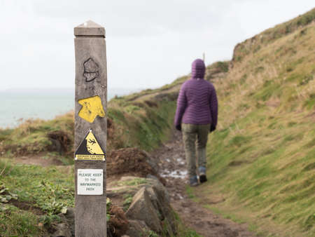 A sign on a coast path shows direction and also warns of danger of falling over unfenced cliff edge....