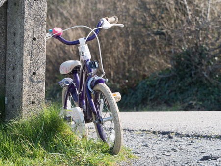 A girl child's bike is leant against a concrete post next to a cycleway.Flower patterns on bike