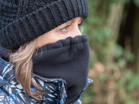 A close up of a lady wearing a black wool hat and snood covering her face with just her eyes showing.She looks ahead and has long hair hanging from under the hatの写真素材